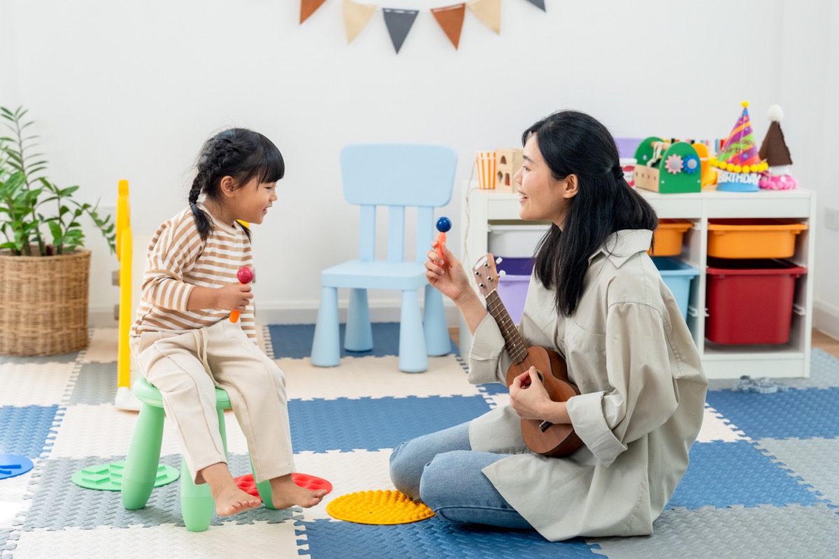 華人媽媽彈著烏克麗麗，幼兒在旁拿著沙鈴唱歌