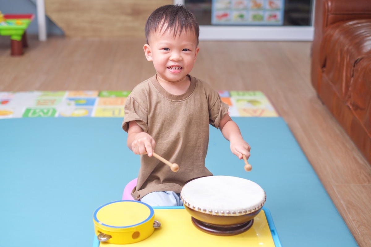 華人幼兒拿著鼓棒敲打小鼓，專心感受節奏
